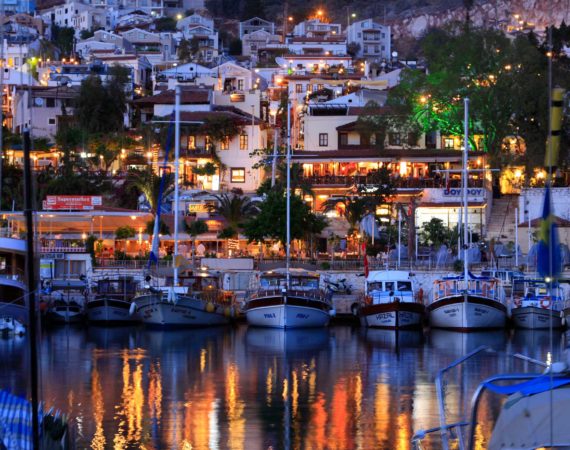 Kalkan harbour at dusk with twinkling lights and bustling rooftop terraces filled with diners overlooking the bay