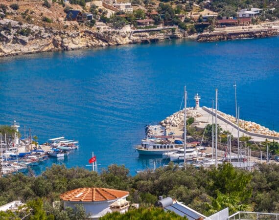 Views from a rooftop terrace overlooking Kalkan Harbour, with whitewashed buildings, moored boats, and the turquoise sea beyond.