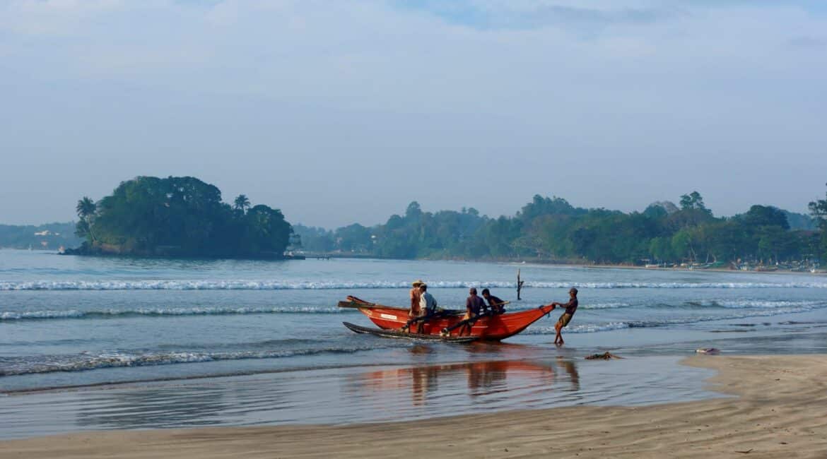 Fishermen bringing in colourful boats on Weligama Beach near Tekanda Lodge, with golden sand, gentle surf, and early morning light on the south coast of Sri Lanka.