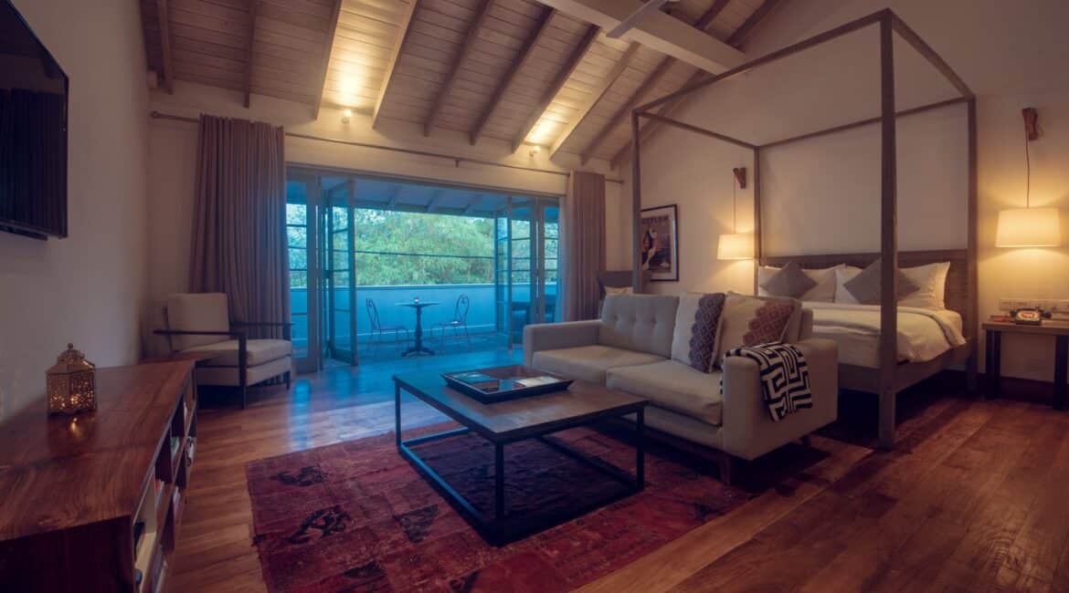 Upper Suite at Fort Bazaar Hotel Sri Lanka showcasing stunning interiors with a king-size bed draped in white linens, elegant wooden furnishings, patterned tile floors, and tall windows framed by colonial-style shutters.