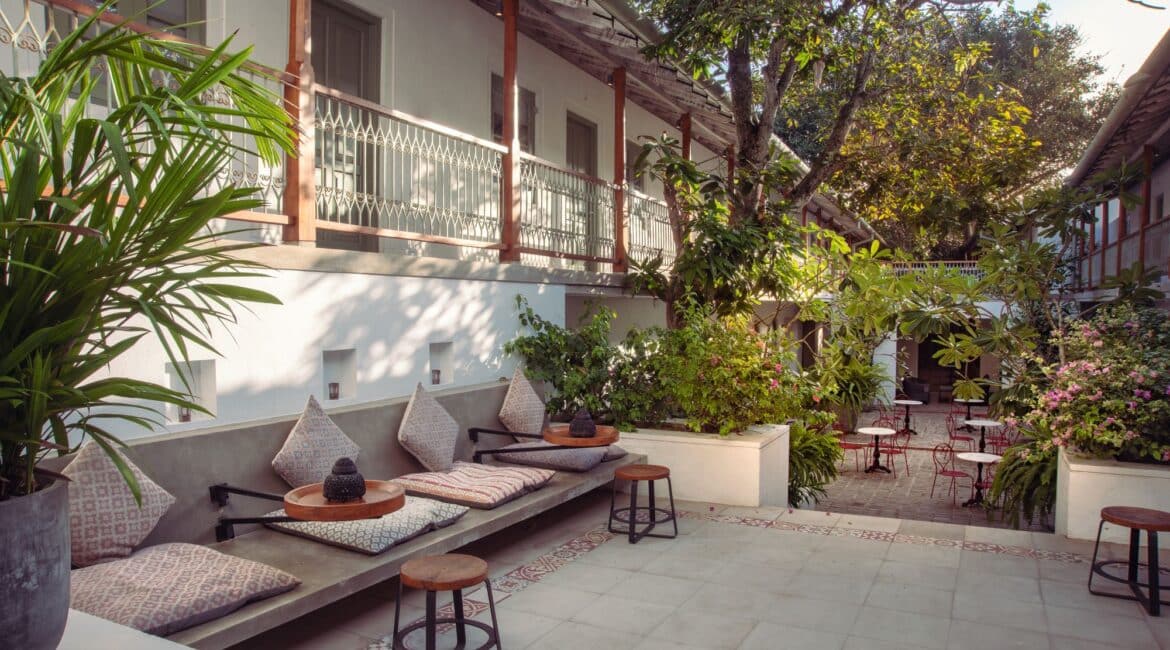 Furnished courtyard at Fort Bazaar Hotel Sri Lanka dappled in shade from the Banyan tree, with comfortable seating and leafy surroundings creating a tranquil setting.