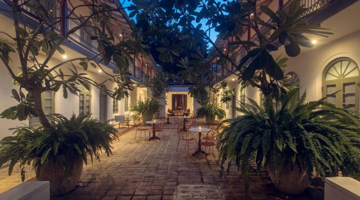 Furnished courtyard at Fort Bazaar Hotel Sri Lanka at dusk, with warm lighting, comfortable seating, and leafy vegetation overhead creating a serene ambiance.