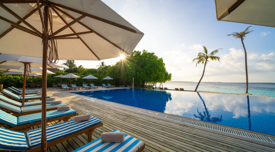 Reethi Faru Resort swimming pool and decked edging with palm trees and ocean views in the Maldives