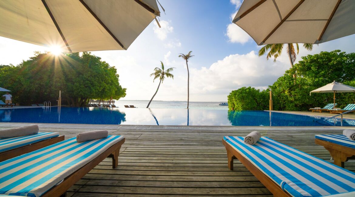 Reethi Faru Resort swimming pool fringed by day beds and Indian Ocean views Maldives