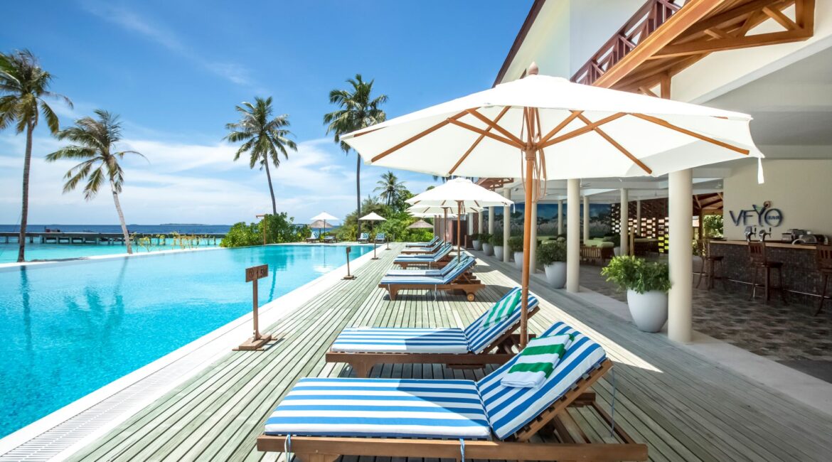 Reethi Faru Resort swimminh pool surrounded by decked sunbathing areas with day beds