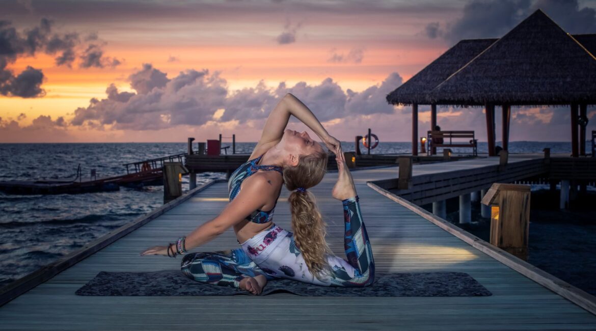 A lady practising Yoga on a dock at sunset at Reethi Faru Resort in the Maldives