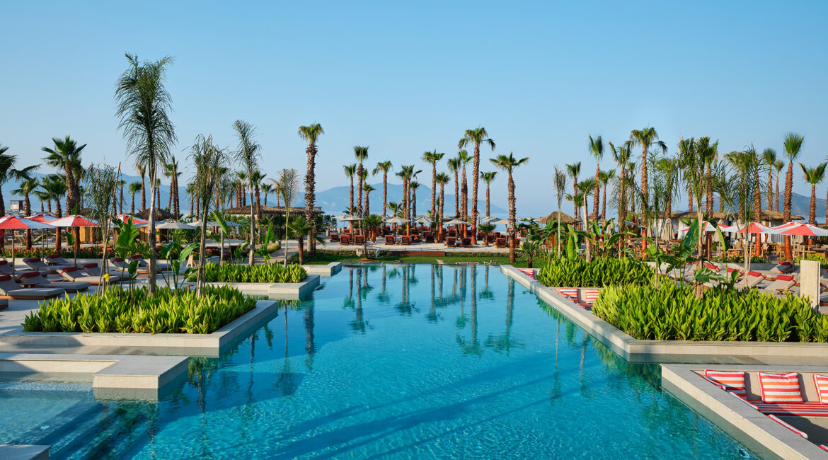 Large outdoor swimming pool surrounded by palm trees at XO Cape Arnna