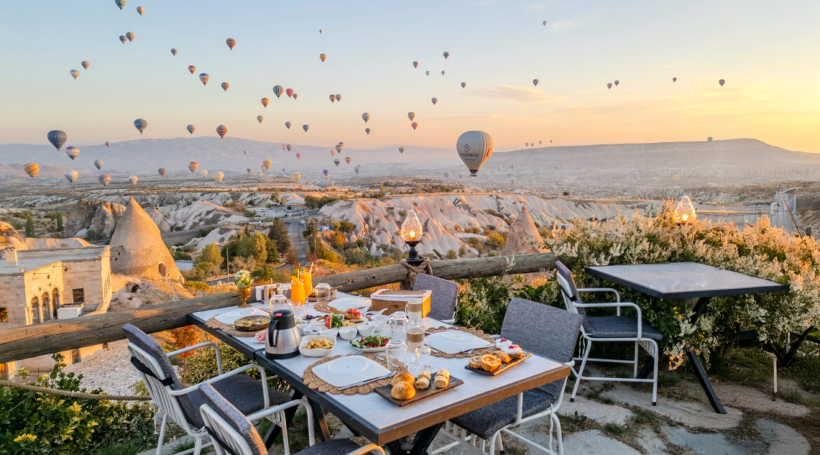 Outdoor breakfast setting overlooking Cappadocia’s valleys with balloons at sunrise