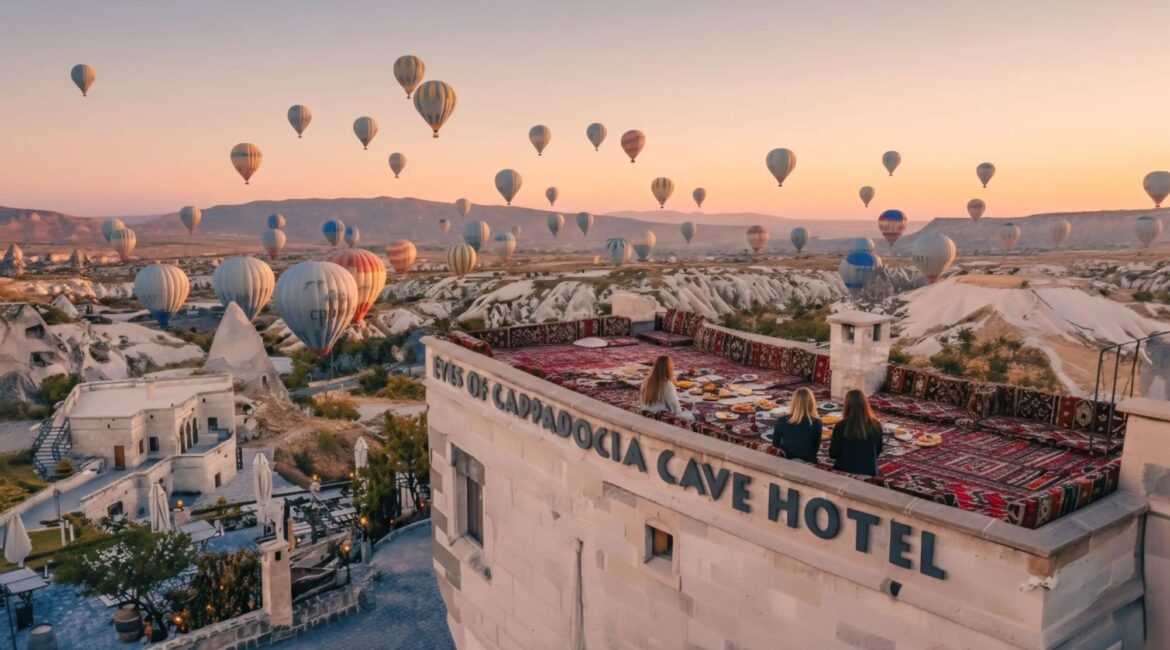 Eyes of Cappadocia Uçhisar terrace with traditional köşk seating overlooking Pigeon Valley and hot air balloons at sunrise