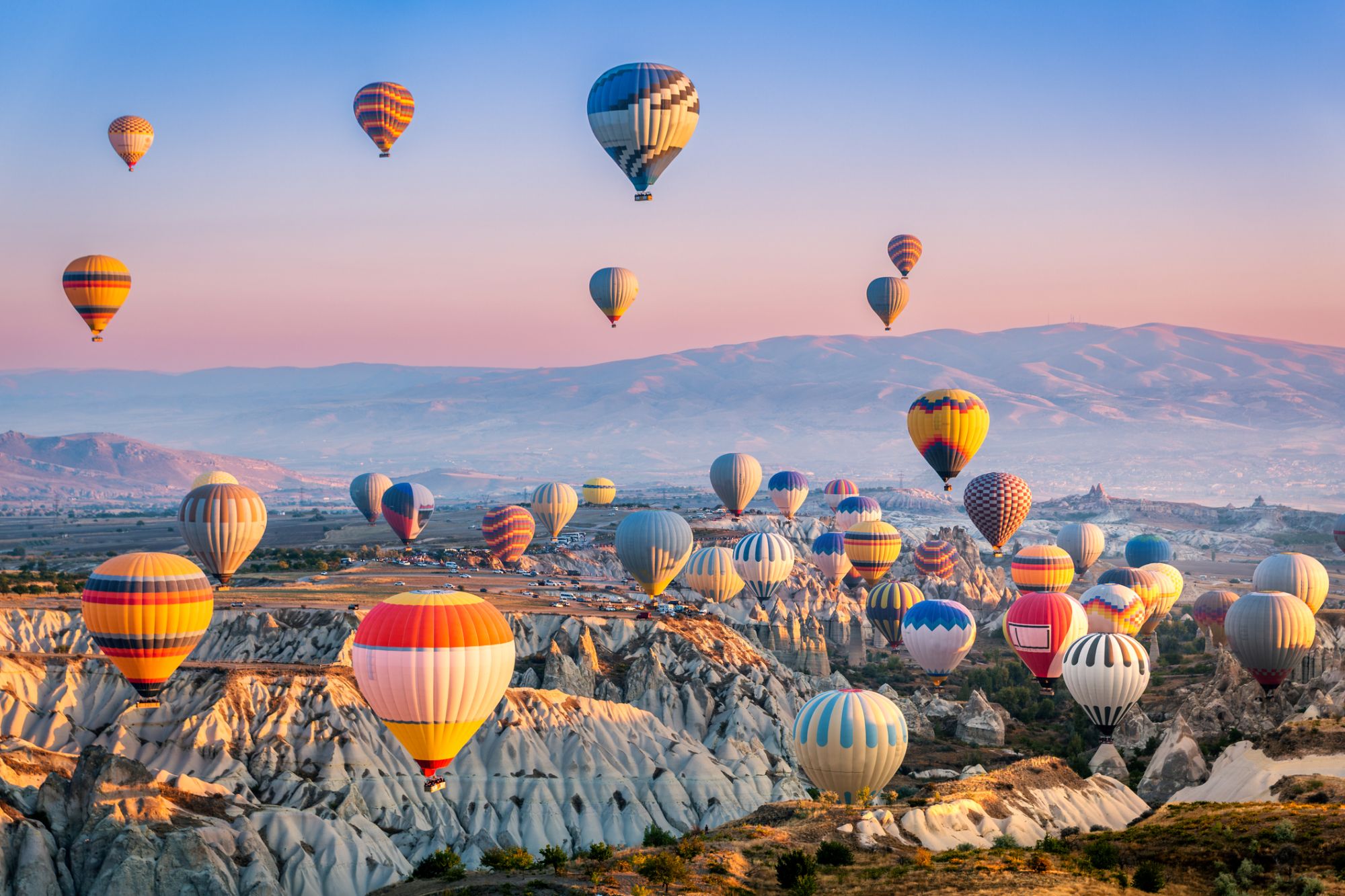 Hot air balloons floating above Cappadocia at sunrise with fairy chimneys and valleys stretching across the Anatolian landscape.